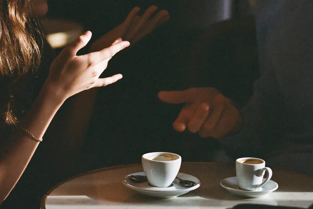 Two people in conversation over espresso at a small cafe table, warm side light